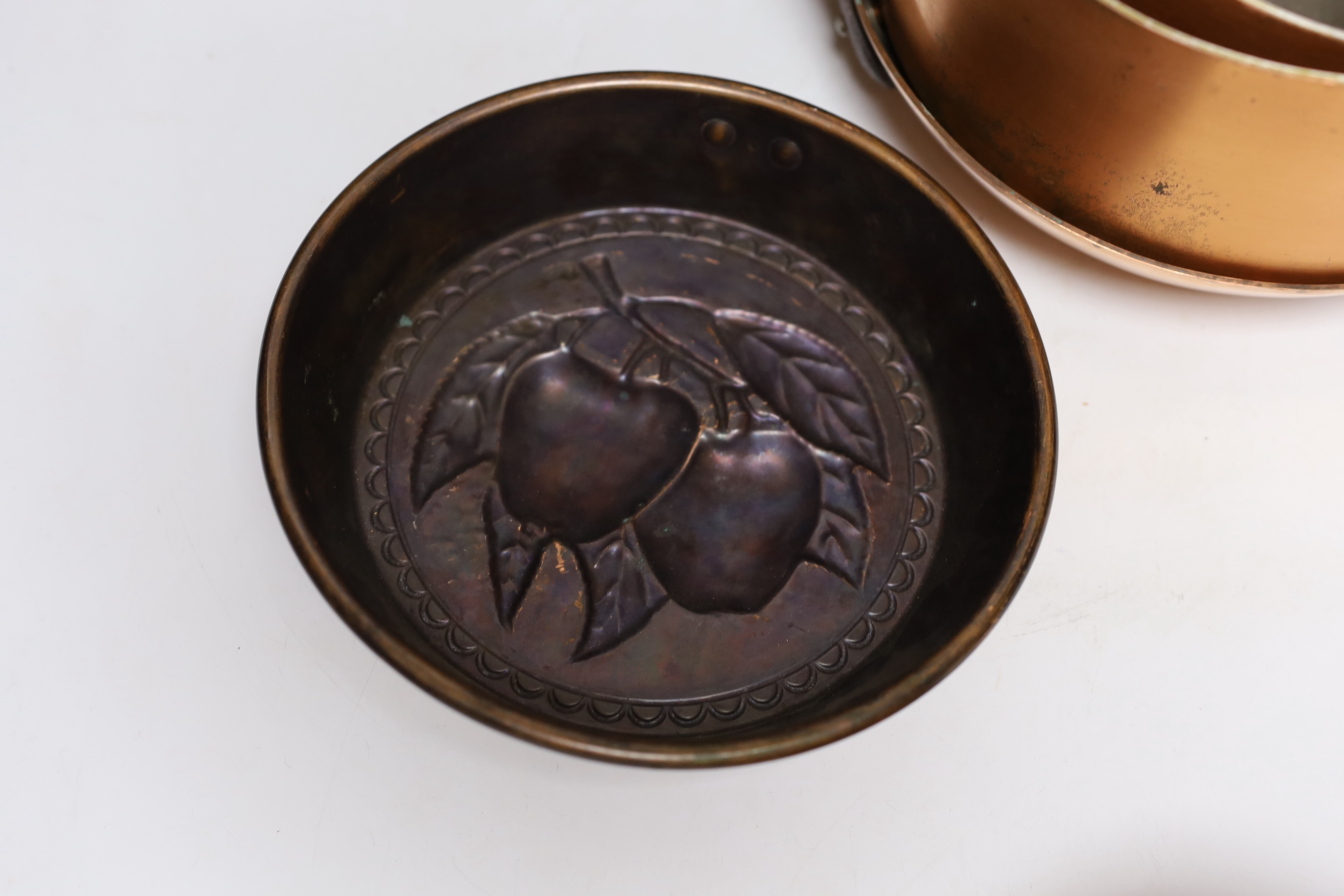 Three copper saucepans, a frying pan, a decorative mould and a pine hanging rack, largest 58cm wide